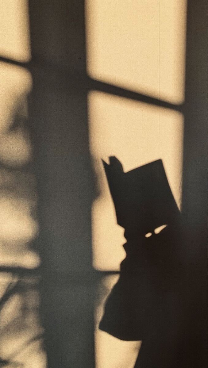 Ombre d'un livre ouvert projetée sur un mur texturé dans une lumière chaude